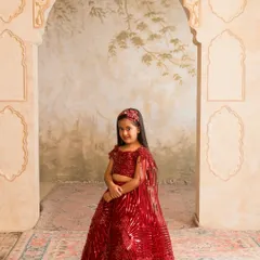 A classic red lehenga is a must have for any festive wardrobe. This custom stitched piece features shimmering sequin work and a delicate cape, ensuring she stands out at any wedding or celebration. We can customize this design in any color you choose.