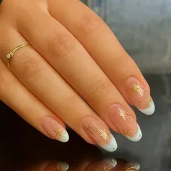 A closer look at a modern French manicure, featuring delicate gold star embellishments and tiny rhinestones for a touch of sparkle.