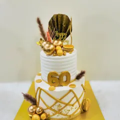 An elegant two-tiered cake for a 60th birthday. The design features clean white frosting, a modern geometric gold pattern, and is topped with dried botanicals and macarons.