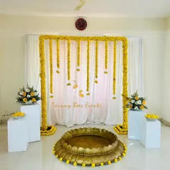 Our simple Haldi setup is perfect for any space. It includes a marigold arch, a large brass Urli for the ceremony, and two white pedestals with floral arrangements to frame the space beautifully.