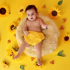 A bright and cheerful studio shot with a vibrant yellow theme. The baby is lying on a soft cushion surrounded by sunflowers, creating a sunny and happy portrait.