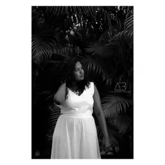 A classic black and white portrait against a backdrop of palm leaves. The contrast between her white dress and the dark leaves creates a striking composition.