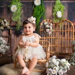 A classic sitter milestone portrait. This baby girl looks so elegant in her white dress, surrounded by a rustic and floral setup.