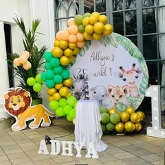 A 'Wild One' jungle theme birthday decoration set up on a patio. The natural greenery and daylight complement the theme, which includes a custom backdrop and a balloon garland in jungle colors.