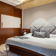 The master bedroom at Rue 32 redefines serenity with a refined palette of greys and natural wood. A commanding bed with a grey upholstered headboard sits beneath a herringbone wooden ceiling, creating a soulful sanctuary for quiet moments.