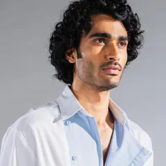 Men's grooming for an editorial shoot, focusing on enhancing the model's natural curly hair texture. The skin is perfected for a matte, even finish under studio lighting.