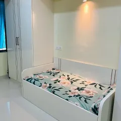 A compact bedroom design featuring a single bed with a built-in headboard and an attached wardrobe. A small wall-mounted light provides a cozy reading spot.