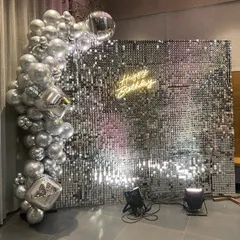 A glamorous bachelorette party setup featuring a full silver sequin shimmer wall. The wall catches the light beautifully and serves as a dynamic photo backdrop, complemented by a silver organic balloon arch and a custom neon sign to personalize the event.