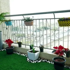 This cheerful balcony garden uses a combination of artificial grass, colorful railing planters, and floor pots to create a vibrant and lively atmosphere. The white pebble border adds a clean, finishing touch.