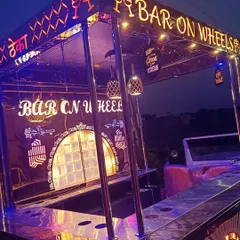 The 'Bar on Wheels' seen at dusk, with its custom lighting and branding illuminated. The setup includes a full bar counter, shelving for spirits, and a distinct look that adds a unique flair to your party.