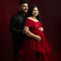 A joyful and elegant couple's portrait. Their bright smiles add a touch of warmth to the dramatic red backdrop and formal attire.