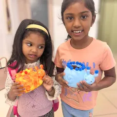 Two young sisters proudly display the adorable animal planters they painted. One is a fiery dinosaur and the other a cool blue snail.