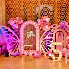 An elaborate butterfly-themed party with a stunning pink and purple color scheme. This setup includes large lighted butterfly wings, a sequin backdrop, a light-up Ferris wheel prop, and a white picket fence for a complete fairytale look.