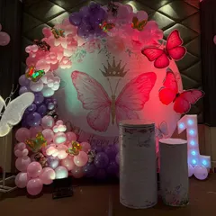 This butterfly-themed first birthday is all about enchantment. I used a circular backdrop with a large butterfly graphic, surrounded by a lush balloon garland in pink and purple, and accented with large 3D butterfly props and a lit-up number '1'.