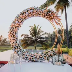 A stunning circular arch decorated with pastel flowers, set against a backdrop of palm trees. This makes for a breathtaking selfie spot for a destination or beachside event.