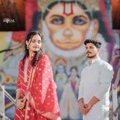 A unique and culturally rich portrait of a couple in traditional wear, posing in front of a vibrant mural of Lord Hanuman.
