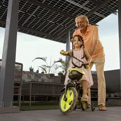 A grandfather helps his granddaughter ride her bicycle under the shade of their new solar panel structure. Our systems are built to protect what matters most, your home and your family.