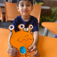 Success! He holds up his finished alien craft, a fun, googly-eyed character. This activity helps develop fine motor skills while reinforcing the creative theme of the day.