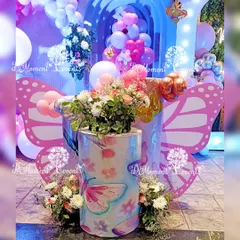 A close-up view of the detailed decor for a butterfly-themed party. This image highlights the custom-printed pedestals with butterfly illustrations, topped with fresh flower arrangements that complement the pink and purple color scheme.