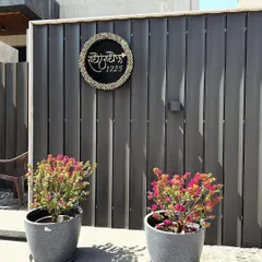 A custom nameplate on a modern slatted wall, flanked by two pots of vibrant bougainvillea, adding a personal touch and a splash of color.