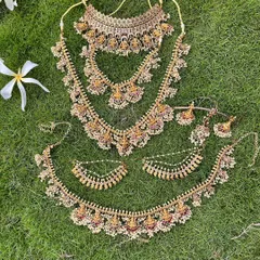 A full view of a temple jewellery set with pearl detailing, laid out on the grass. This shows the choker, two haarams, and the vaddanam.