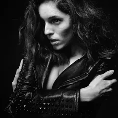 A close-up portrait in black and white. The lighting is carefully sculpted to create deep shadows and bright highlights, emphasizing the texture of the leather jacket and the intensity in her eyes. This is what I call grit.