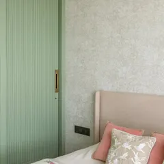 A detail from the bedroom, where a soft mint green fluted wardrobe door adds a gentle pop of color. This is paired with a delicate floral wallpaper and pastel pink cushions for a soft, romantic feel.