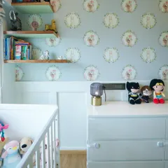 A close-up of the nursery's feature wall, which has a charming custom wallpaper of illustrated pets. The floating shelves are perfect for displaying books and favorite toys.