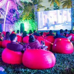 A wide shot of our open-air cinema setup, with guests relaxing on beanbags under the purple-lit palm trees.