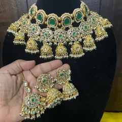 A complete view of our green stone choker set, held to show the matching maang tikka and earrings. This is a versatile piece that can be worn by the bride or by family members for a coordinated wedding look.