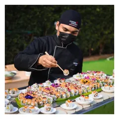 A chef meticulously prepares a platter of assorted vegetarian sushi rolls, garnished with edible flowers, for a beautiful day reception. We cater to all dietary preferences with creativity.