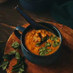 A comforting bowl of Daleem, a traditional slow-cooked stew, garnished with fresh herbs. The moody lighting and rustic wooden board create a warm and hearty feel, perfect for showcasing traditional cuisine.