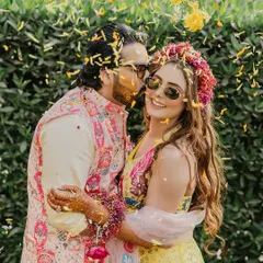 A sweet, candid moment with the groom kissing the bride's cheek amidst a shower of petals during their Haldi ceremony.