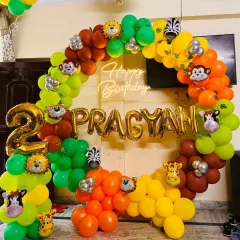 A full view of a jungle-themed birthday party setup. The large circular frame is the centerpiece, wrapped in a vibrant balloon arch with pops of green, orange, and yellow, and accented with fun animal characters and a custom name display.