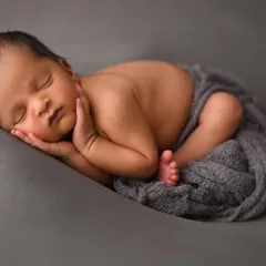 The perfect, peaceful newborn pose. As a certified newborn photographer, I ensure your baby is safe and comfortable to capture these sleepy, curled-up moments. This classic shot on a simple grey backdrop highlights the delicate features of this sweet baby boy.