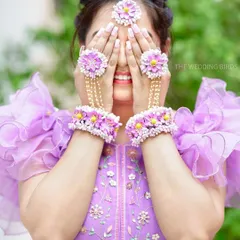 A playful mehendi portrait. The bride hides her smiling face behind her hands, showing off her beautiful floral jewelry and the joy of the occasion.