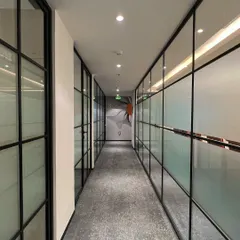 A corridor in the Rays Power office lined with glass-walled cabins. The use of frosted and clear glass panels provides privacy while still allowing natural light to flow through the space, creating a sense of openness.