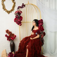 For a touch of glamour, I use setups like my golden birdcage chair, adorned with rich, deep red flowers. This portrait showcases a bold and elegant style, celebrating the mother-to-be in a truly regal way.