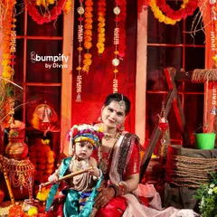 A classic portrait of mother and child. Here, our little Krishna sits peacefully in his mother's lap, creating a beautiful memory against the rich, red Janmashtami setup.