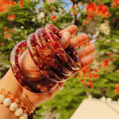 A set of custom bangles made from preserved red flowers and gold flakes encased in clear resin. Each piece is unique and handcrafted.