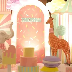 A close-up of the candyland setup, with a tall giraffe prop, a tiered cake, and a giant macaron, all in soft pastel colors.