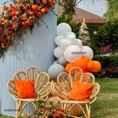 A detail shot of the custom wicker chairs and floral arrangements from the "Tangerine & Twinkles" baby shower. The combination of fresh flowers, real oranges, and natural textures creates a unique and stylish photo corner.