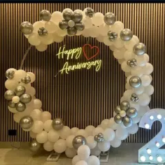 A close-up of a white and silver anniversary balloon ring with a 'Happy Anniversary' neon sign.