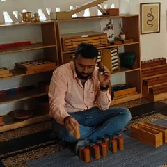 A parent works with the Knobbed Cylinders, a foundational Montessori material for visual discrimination. This activity refines the senses and prepares the hand for writing, and you get to feel the deep concentration it inspires.