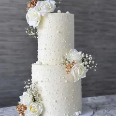 A classic and timeless two tier wedding cake. The simple design with pearl dot details is elevated by clusters of beautiful white roses, creating a look of pure elegance.