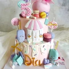Welcome to Candyland. This cake is a dream for any sweet tooth, decorated with an assortment of edible treats like lollipops, macarons, cakesicles, and chocolate bars, all arranged to create a magical candy shop scene for a fifth birthday.