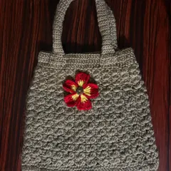 A sturdy, hand-crocheted tote bag in a neutral beige color, accented with a bright red and yellow flower for a pop of color.