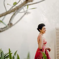 A beautiful candid of the bride, Jisha, walking through a garden, her pink lehenga vibrant against the green foliage.