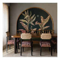 This dining space is defined by a custom-commissioned, hand-painted tropical mural. We designed the dining table and chairs with natural cane and printed fabric to complement the artwork, creating a conversational and artistic corner in the home.