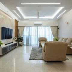 This living room at SNN Clermont combines comfort and luxury with plush beige recliners and a stunning TV wall. We used a combination of a marble-textured panel and geometric wood paneling, complemented by linear ceiling lights to create a warm, contemporary feel.